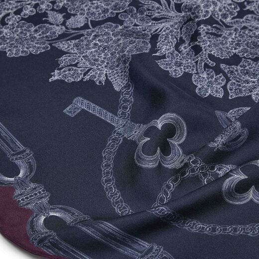 Close up of a blue scarf with a print featuring an ornate key and details of jewellery.
