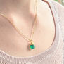 Close up of a white woman's neck wearing a gold chain necklace with a green pendant.